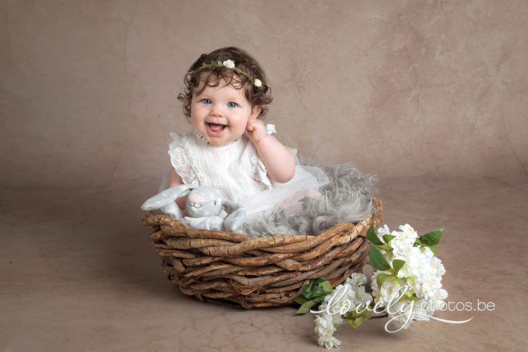 Lachende baby in een rieten mandje met witte bloemen – babyfotoshoot Hasselt