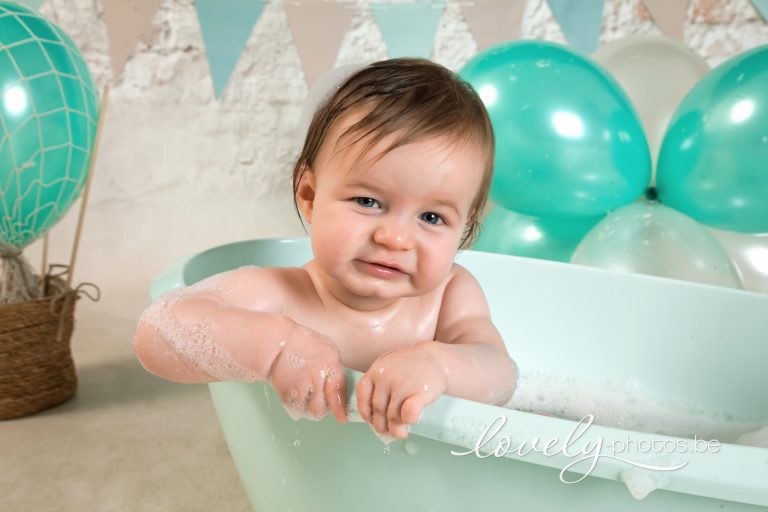 Lachende baby in een mintgroen badje met ballonnen – cake smash splash fotoshoot