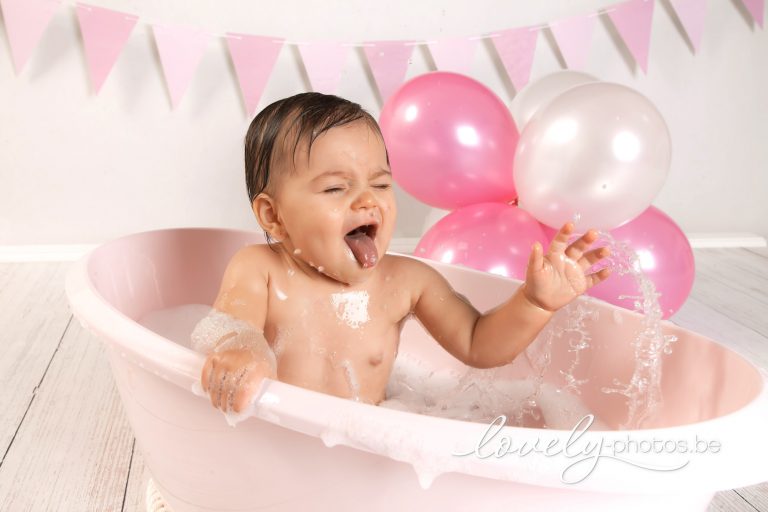 Lachend meisje speelt in een roze badje met ballonnen – cake smash splash shoot Hasselt