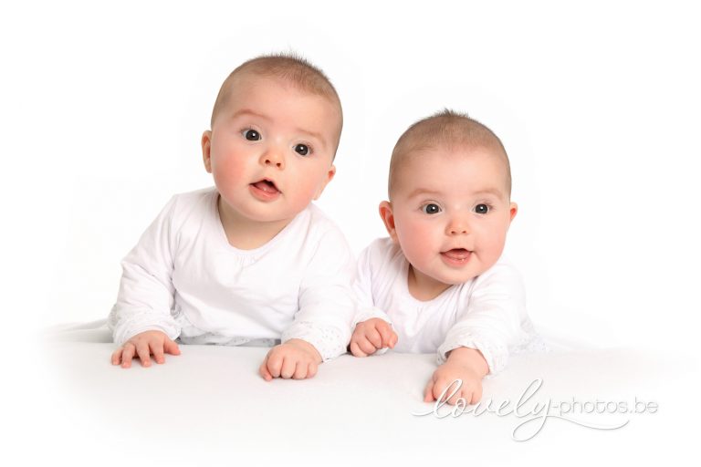 Babytweeling in witte pakjes ligt op de buik – tweeling babyfotoshoot Hasselt