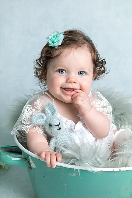 Lachend babymeisje met mintgroen bloemetje in het haar zit met een gehaakt konijntje in een mintgroen badje – babyfotoshoot Hasselt