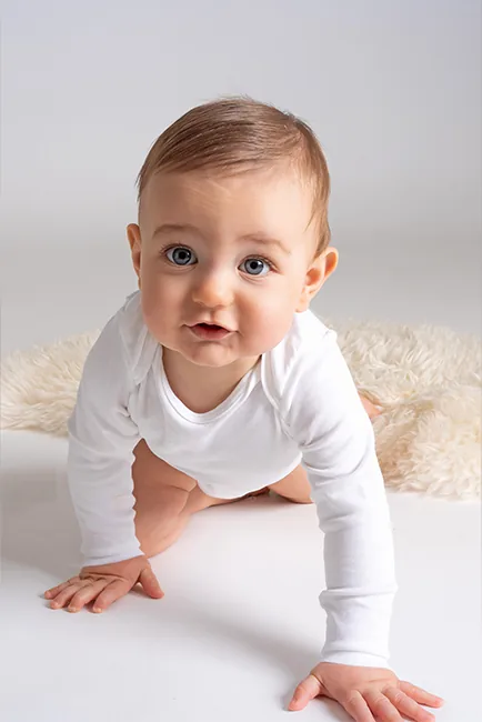 Baby in wit rompertje kruipt nieuwsgierig naar de camera op een wit vachtje – Little Star babyfotoshoot in Hasselt