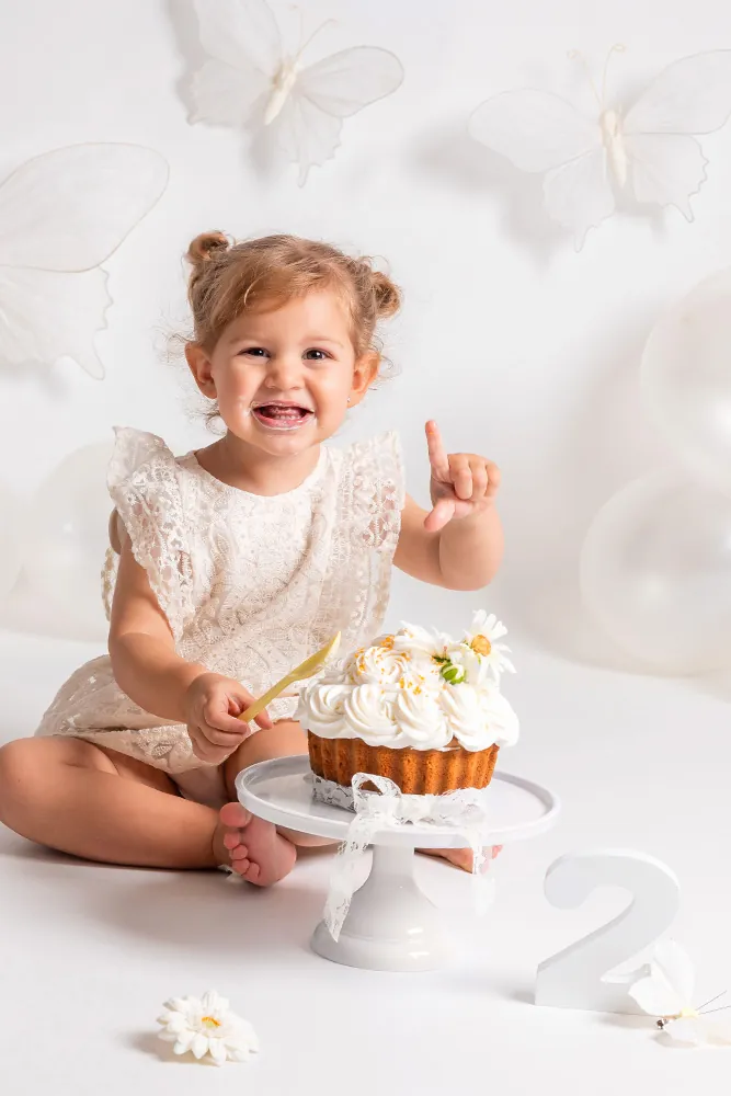 Lachend meisje van twee jaar met witte bloementaart tijdens haar cakesmash in de fotostudio