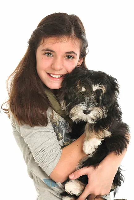 Lachend tienermeisje knuffelt haar zwart-witte pup tegen een witte achtergrond – familiefotoshoot met huisdier in Hasselt